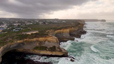 Drone görüntüleri, Avustralya, Port Campbell 'daki dramatik uçurumları ve çalkantılı denizleri, dinamik kamera hareketiyle bulutlu gökyüzünün altında yakalıyor.