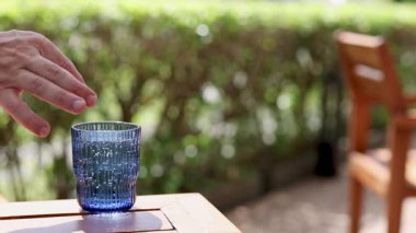 Bir el açık hava masasında mavi bir bardak sodanın içine limon sıkıyor.