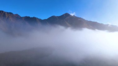 A serene view of fog rolling over mountains at Moke Lake, Queenstown. Clear blue sky contrasts with the misty landscape