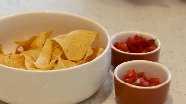 Hands adding salsa to chips in a bowl