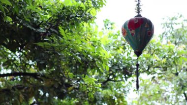 Traditional lantern sways amidst lush green foliage.