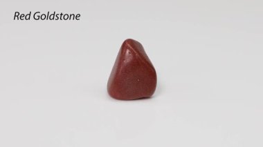 Kırmızı bir altın taşı beyaz bir yüzeyde döner..