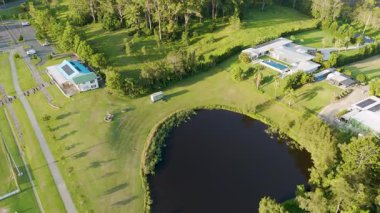 İnsansız hava aracı görüntülerinde geniş yeşil manzaralar, sakin bir göl ve açık gökyüzünün altındaki uzak şehir silueti görülüyor.