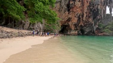 Turistler bir kayalık mağaranın yakınında bir plajın keyfini çıkarırlar.