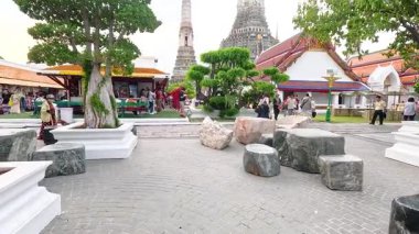 Ziyaretçiler Bangkok 'taki Wat Arun tapınağını keşfediyor, parlak gün ışığında canlı mimari ve bereketli yeşillik sergiliyorlar.