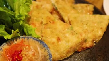 Bir el taze yeşillik ve ahşap bir masada sosla servis edilen çıtır karides krepine uzanır.