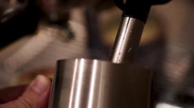 Buhar çubuğu, sıcak ışık ve sabit kamera ile paslanmaz çelik bir sürahide köpüren sütün yakın çekimi.