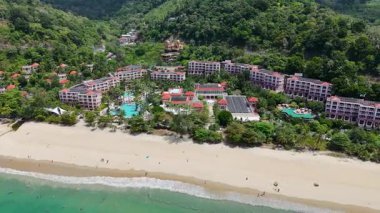 İnsansız hava aracı görüntülerinde verimli bir Phuket tatil köyünün manzaralı bir üstgeçişi görülüyor. Canlı yeşillikler, kumlu plajlar ve turkuaz havuzlar sergileniyor.