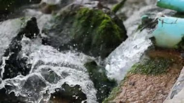 Su yosunlu drenaj sisteminden geçer, sıçramalar ve hareketler yaratır. Doğal ışıklandırma yeşil yosunları ve akan suyu vurgular