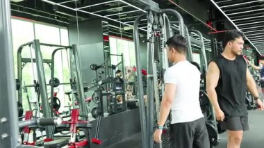 İki adam, iyi aydınlatılmış bir spor salonunda kablo kullanırlar. Güç antrenmanlarına odaklanırlar.