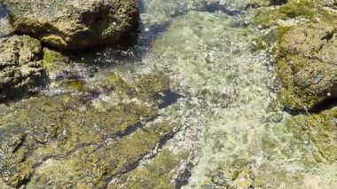 Dalgalar yavaşça Yanui Sahili, Phuket 'te kayalık bir gelgit havuzunun üzerinde süzülür, suyun ve güneşin dingin hareketini yakalar.