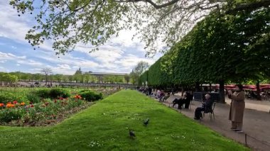 Çiçeklerle dolu bir parkta güneşli bir günün tadını çıkaran ziyaretçiler