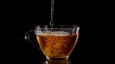 Şeffaf cam bardağa dökülen bir çay dizisi koyu bir arkaplan karşısında, sıvının zengin rengini vurguluyor.