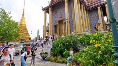 Turistler, Bangkok, Tayland 'daki canlı Wat Phra Kaew Tapınağını gün ışığında keşfederek, tapınağın karmaşık mimarisini ve bereketli çevresini yakalıyorlar.