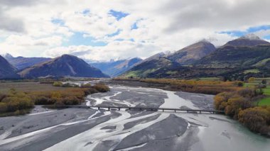 Glenorchy 'de parçalı bulutlu bir gökyüzünün altında, verimli vadiler ve dağlardan geçen dolambaçlı bir nehrin havadan görünüşü