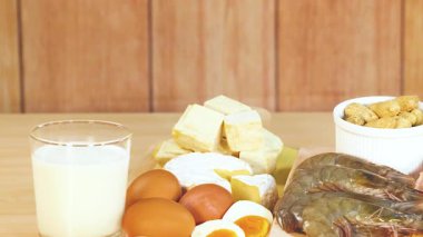 Süt ürünleri, fındık ve etler de dahil olmak üzere çeşitli protein zengini gıdalar parlak ışıklandırılmış ahşap bir masada sergilenir.