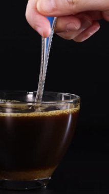 Bir el, bir bardak çaya şekeri karıştırır ve siyah bir arka plan oluşturur.