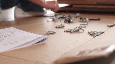 Eller ahşap bir masada montaj talimatları ile donanım organize eder. Parlak ışıklandırma ayrıntılı süreci vurgular