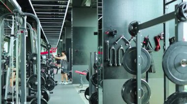 Bir insan, modern ekipmanlarla dolu, odaklanmış ve enerjik bir atmosfer yaratan, parlak ışık altında iyi donanımlı bir spor salonunda egzersiz yapar.