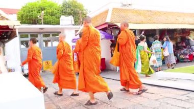 Turuncu cüppeli keşişler Bangkok, Tayland 'da canlı market tezgahlarının önünden geçiyorlar. Parlak gün ışığı hareketli sahneyi aydınlatıyor.