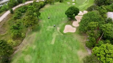 İnsansız hava aracı görüntüleri Phuket, Tayland 'daki yemyeşil bir sahada golfçüleri yakalıyor, canlı manzaralar ve stratejik kum sığınakları sergiliyor.