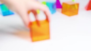 Eller, beyaz bir yüzey üzerinde canlı üç boyutlu geometrik şekilleri manipüle eder, parlak, eğitici bir ortamda şekil ve renkleri keşfederler.