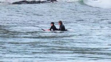 Hoca bir çocuğa sörf yapmayı öğretiyor.
