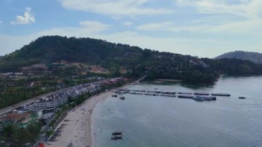 İnsansız hava aracı görüntüleri Patong Sahili 'nin sahil şeridini uzun kuyruklu tekneler ve tatil beldeleri ile görüntülüyor, dingin okyanusu ve verimli tepeleri gün ışığında gösteriyor.