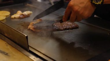 Aşçı ustalıkla ızgarada biftek hazırlar.