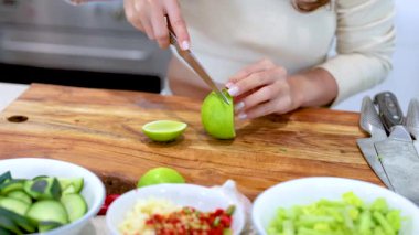 Bir insan, parlak bir mutfakta taze salata malzemeleriyle çevrili ahşap bir tahtada limon dilimler.