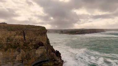 Port Campbell, Victoria, Avustralya 'da bulutlu gökyüzü altında engebeli uçurumların ve çalkantılı okyanus dalgalarının hava manzarası.