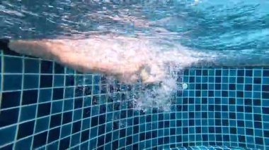 Bacaklar su altında hareket ediyor, havuzda kabarcıklar oluşturuyor.