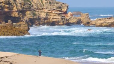 Yalnız bir insan kumlu bir sahilde duruyor, açık gökyüzünün altında okyanus dalgalarına bakıyor.