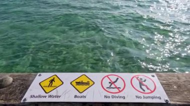 Rıhtımdaki uyarı işaretleri sığ sularda dalış ve tekneye karşı güvenlik önlemlerini vurguluyor