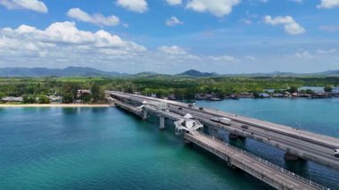 İnsansız hava aracı görüntülerinde Phuket, Tayland 'daki Sarasin Köprüsü açık bir gökyüzü altında turkuaz sulara yayılıyor. Araçlar manzaralı yoldan geçiyor