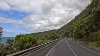 Yeşillik ve dolambaçlı yollarda parçalı bulutlu bir gökyüzünün altında sakin bir sürüş yakalayan 14 saniyelik bir video.