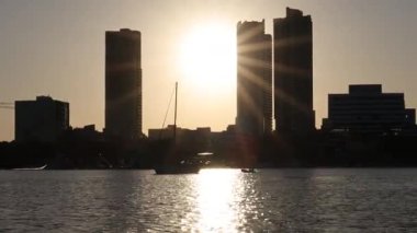 Güneş binaların arkasında batıyor, suyu yansıtıyor.