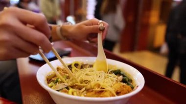 Yemek çubuğu ve kaşıkla erişte çorbası içen biri.