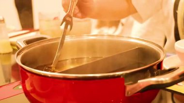 Şef sıcak kapta kepçeyle sukiyaki hazırlıyor.