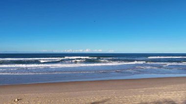 Dalgaların hava görüntüleri, açık mavi gökyüzünün altında, Sörfçüler Cenneti 'nin kumlu sahillerine yavaşça iniyor.