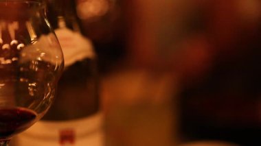 Yakın plan şarap kadehleri ve şişeler loş, ılık bir ortamda rahat ve samimi bir atmosfer yakalıyor.