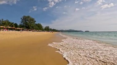 Yumuşak dalgalar, sakin bir Phuket plajının kumlu sahilinde, yumuşak günbatımı ışığı altında, barışçıl bir atmosfer yaratır.