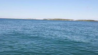 Yumuşak dalgalar ve açık gökyüzü altındaki uzak adalar