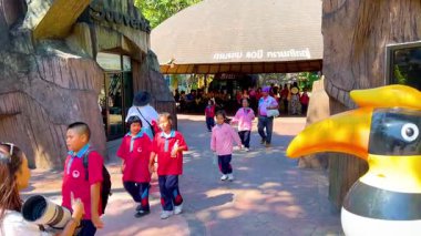 İnsanlar hayvanat bahçesine giriyor, güneşli bir günün tadını çıkarıyor.