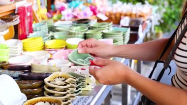 Tayland, Phuket 'teki hareketli bir sokak pazarında canlı seramik yemekleri inceleyen bir insan. Parlak ışıklandırma renkli görüntüyü güçlendirir