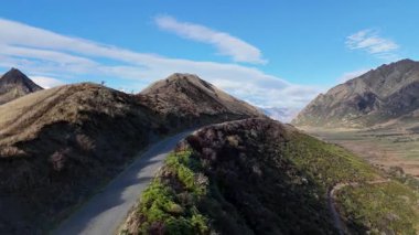 Hava görüntüleri, açık mavi gökyüzünün altında Queenstown, Yeni Zelanda 'daki dolambaçlı dağ yolları ve çarpıcı manzaraları yakalıyor.