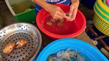 Kırmızı kasede deniz salyangozlarını temizleyen kişi