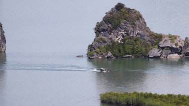 Tayland, Phang Nga 'daki kayalık bir adanın yakınındaki sakin sularda süzülen küçük tekneler. Huzurlu sahne doğal güzellik ve hareketi yakalar.