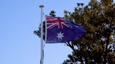 Avustralya bayrağı açık mavi gökyüzüne ve Bellarine, Victoria 'da ağaçlara karşı dalgalanıyor. Sabit kamerayla doğal gün ışığında yakalanmış.