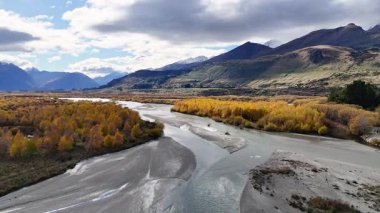 Sonbahar yaprakları arasında dönen bir nehrin hava manzarası. Arka planda dağlarla. Parçalı bulutlu gökyüzünün altında.